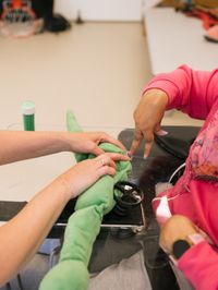 Persoon in rolstoel doet oefening met vingers met behulp van een groene slangachtige rol samen met een ander persoon
