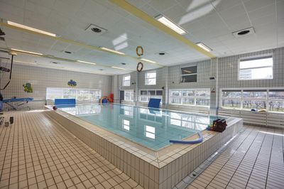 Binnenzwembad met betegelde vloer en wanden, ramen aan één kant en kleurrijke zwemspullen verspreid over het terrein.