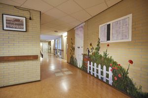 Gang met vrolijke schildering met wit tuinhek, regenton, waterpomp, zonnebloemen, groen en klaprozzen