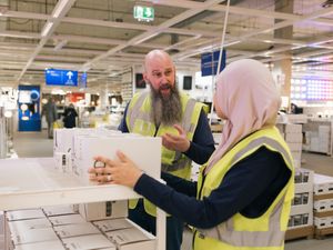Twee personen met gele hesjes zijn in gesprek op de lampenafdeling van een winkel.
