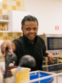 Persoon pakt keukengereedschap en kijkt daarbij lachend in de camera