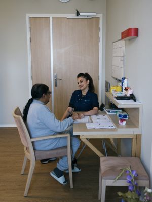 Twee personen met lang donker haar zitten aan een tafel en wijzen naar papieren die op tafel liggen. Ze lachen naar elkaar.