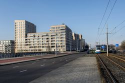 Groot appartementencomplex naast een fietspad en treinrails