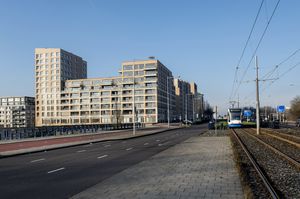 Groot appartementencomplex naast een fietspad en treinrails