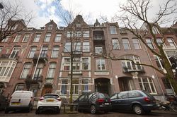 Een Amsterdams pand met vijf verdiepingen met daarvoor geparkeerde auto's.