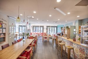 Gezellig restaurant met tafels en stoelen en een grote raam. De bar is versierd met een gekleurde tegelprint.