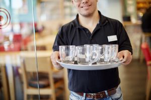 Een man met zwarte polo met in zijn hand een dienblad met vijf theeglazen.