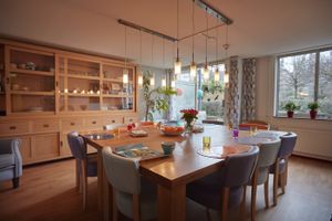 Gezamenlijke ruimte met vierkante eettafel gedekt voor 10 personen met placemats en drinkbekers