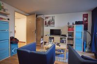 Woonkamer met kasten en tv een zitje met twee blauwe stoelen en een salontafel