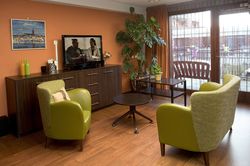 Zitgelegenheid in woonkamer bij het raam met twee stoelen, 2 tafeltjes, een lage wandkast en een grote plant in de hoek