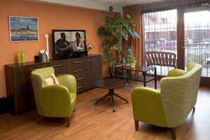 Zitgelegenheid in woonkamer bij het raam met twee stoelen, 2 tafeltjes, een lage wandkast en een grote plant in de hoek