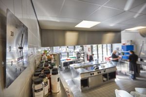 Een grote restaurantkeuken met een klok aan de muur en een plank met allerlei verschillende kruiden.