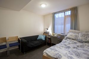 Een slaapkamer met witte muren en tweepersoonsbed, bureau en zwarte bank.