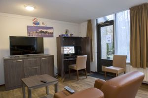 Een woonkamer op benedenverdieping met een zithoek met bruine meubels en een computerkast met computerscherm dat aan staat.