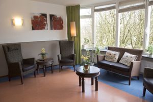 Woonkamer met grote erker die uitkijkt op het Kastanjeplein. Comfortabele stoelen en bank.