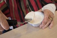 Iemand schept met een aangepaste lepel yoghurt uit een bakje