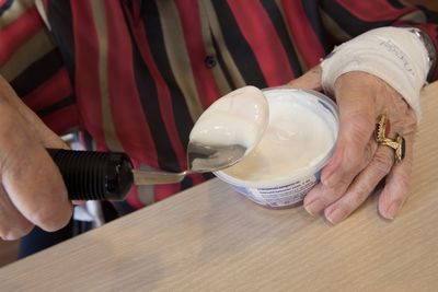 Iemand schept met een aangepaste lepel yoghurt uit een bakje