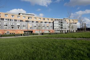 Langwerpig groot gebouw met 5 etages en oranjerode eerste etage staat in een groen park.