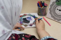 Vrouw met hoofddoek kleurt een mandala in met kleurstiften.