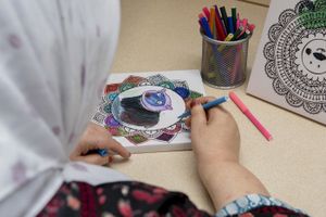 Vrouw met hoofddoek kleurt een mandala in met kleurstiften.