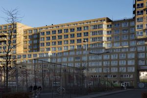 Langwerpig gebouw van 11 etages met veel ramen en een sportveld ervoor.