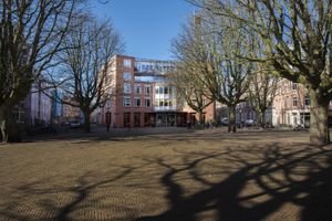 Vooraanzicht van een gebouw met rode bakstenen, vier verdiepingen aan een groot plein.