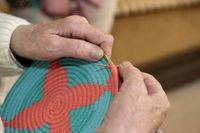 Close up van iemand die een kleurige mand maakt met draad en riet.