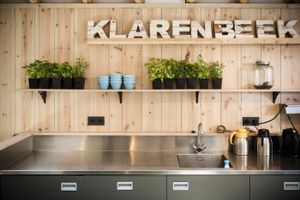 Keuken met gootsteen en koffiekannen, met daarboven een plank met planten en houten letters 'Klarenbeek'..