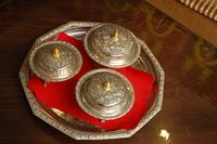 Close up van een mooi versierde zilverkleurige schaal met daarop een rode servet en 3 versierde schaaltjes met deksel in dezelfde stijl.