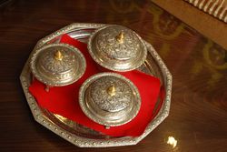 Close up van een mooi versierde zilverkleurige schaal met daarop een rode servet en 3 versierde schaaltjes met deksel in dezelfde stijl.