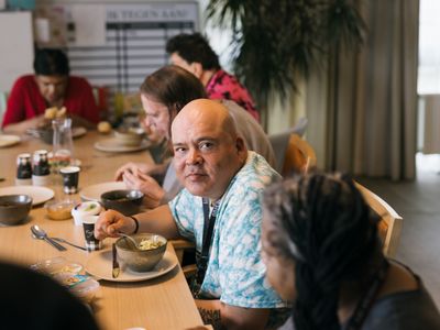 5 personen zitten met elkaar aan een lange tafel te eten