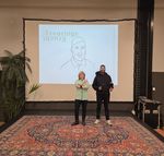 Een man en vrouw staan met hun duim omhoog in een kamer met groot tapijt voor een beamer. Op de beamer staat het logo van Buro Ervaringskracht.