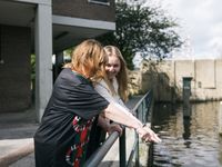 Twee dames lachen, houden groende railing vast en wijzen naar het water