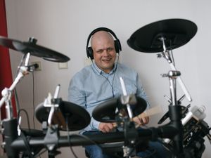 Iemand zit lachend met koptelefoon achter een drumstel en drumt.