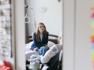 Een jonge vrouw met blond haar zit op een bed tegenover een oudere vrouw. Ze zijn in gesprek.