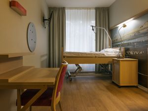 Een kamer met bruine meubels en een hoog-laag bed. Op de muur een grote poster met een strand met vogels.