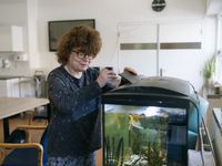 Iemand staat voor een groot aquarium en voert de vissen.