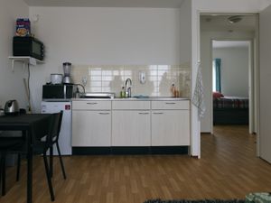 Appartement met zicht op keuken met eettafel en doorkijk door gang naar slaapkamer met bed