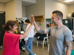 Een gespierde man met tatoeages geeft een high five aan een vrouw met een felroze shirt.