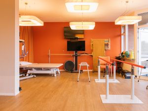 Een lichte ruimte met veel lampen aan het plafond, een rode muur en beweegapparaten.