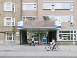 Een gebouw met drie verdiepingen met een brede ingang door het gebouw heen. Daarboven staat een bord met 'Nieuw Vredenburgh', het logo van Cordaan en een pijl en tekst 'St. Augustinuskerk'.