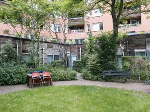 Een groene binnentuin van een appartementengebouw. Er staan een bankje, tafel en stoelen.