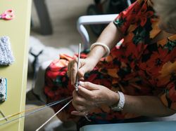 Je ziet van bovenaf een vrouw in een oranje bloemenjurk haken aan tafel.