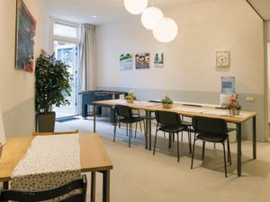 Een lichte ruimte met eettafels en zwarte stoelen. Achterin de ruimte bij een open deur naar buiten staat een voetbaltafel.