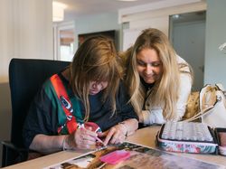 Lachende dame kijkt bij andere dame over haar schouder hoe ze aan het diamond painten is