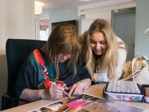 Lachende dame kijkt bij andere dame over haar schouder hoe ze aan het diamond painten is