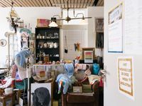 Een volle kamer met veel tweedehands spullen zoals kleding, servies en speelgoed. In het midden staat een balie met oude kassa.