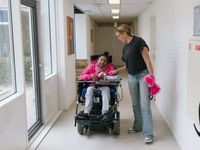 1 persoon staat met iemand in een rolstoel te praten in de gang