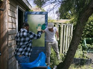 Twee mensen werken in de tuin. Ze staan vóór een tuinhuisje en geven elkaar een high five.