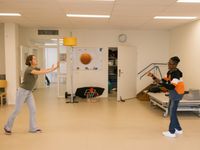 In een sport- of beweegruimte zijn twee personen een bal naar elkaar aan het overgooien